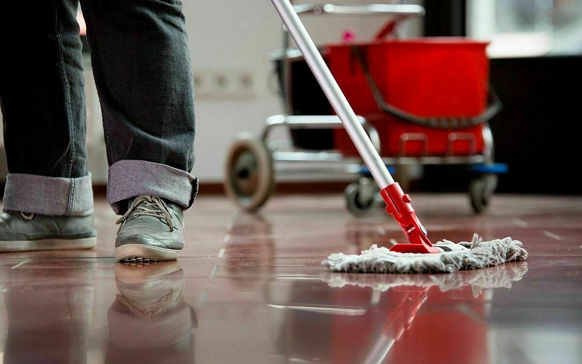Eine Reinigungskraft putzt mit einem Wischer Eine Reinigungskraft putzt mit einem Wischer